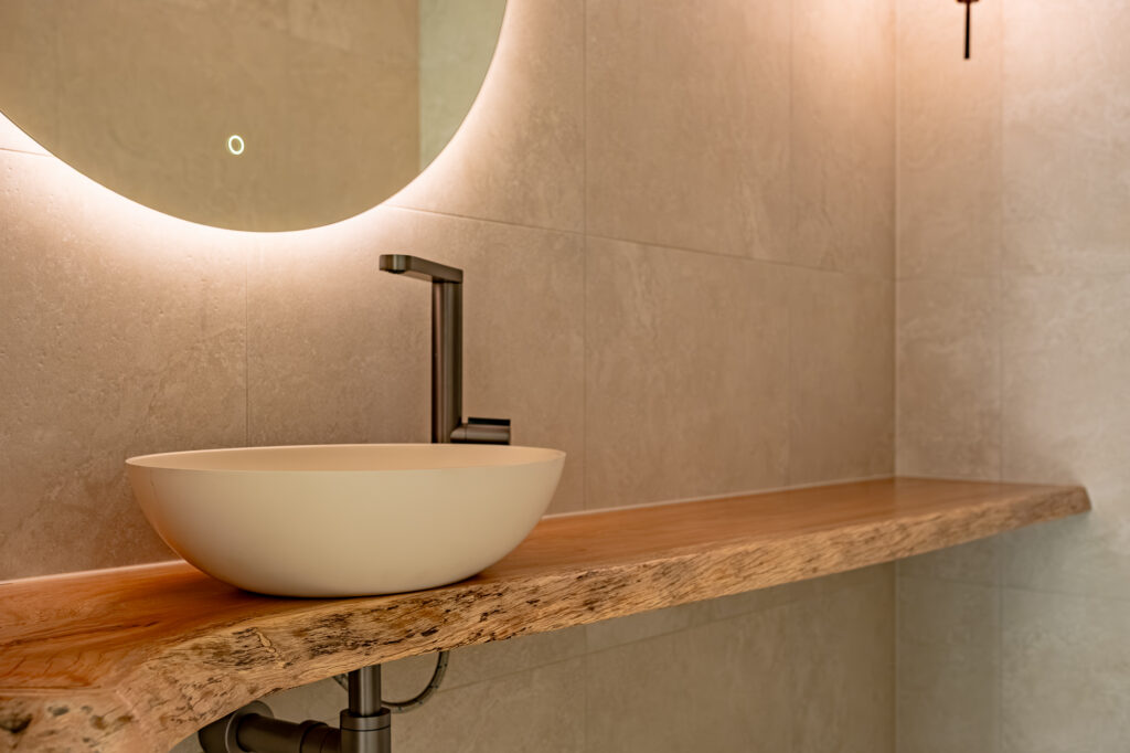 Stone basin on a timber vanity with a backlit round mirror